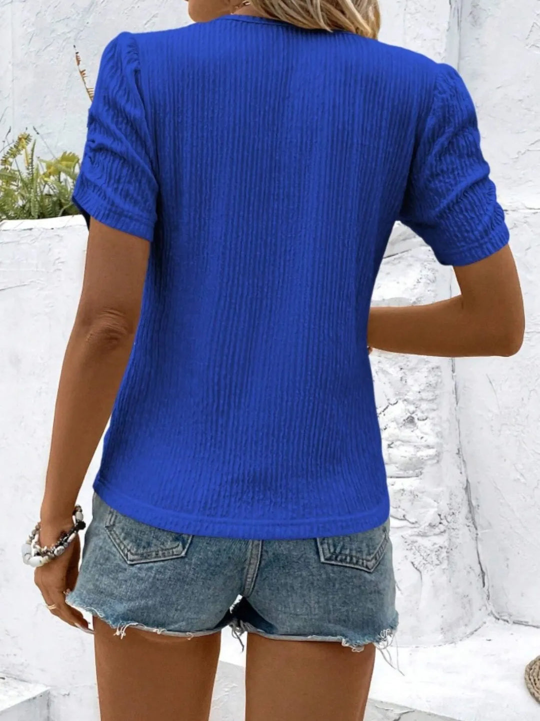 Model in a blue ruched short sleeve top, pairing this fitted women's blouse with casual jeans.
