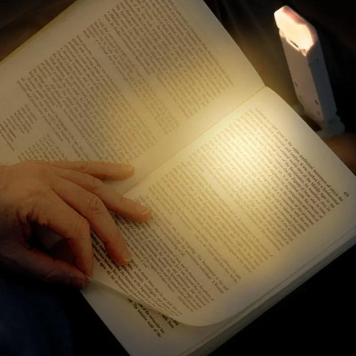 Nvroome clip-on book lamp in use, attached to a paperback, illustrating its hands-free, dimmable LED illumination.