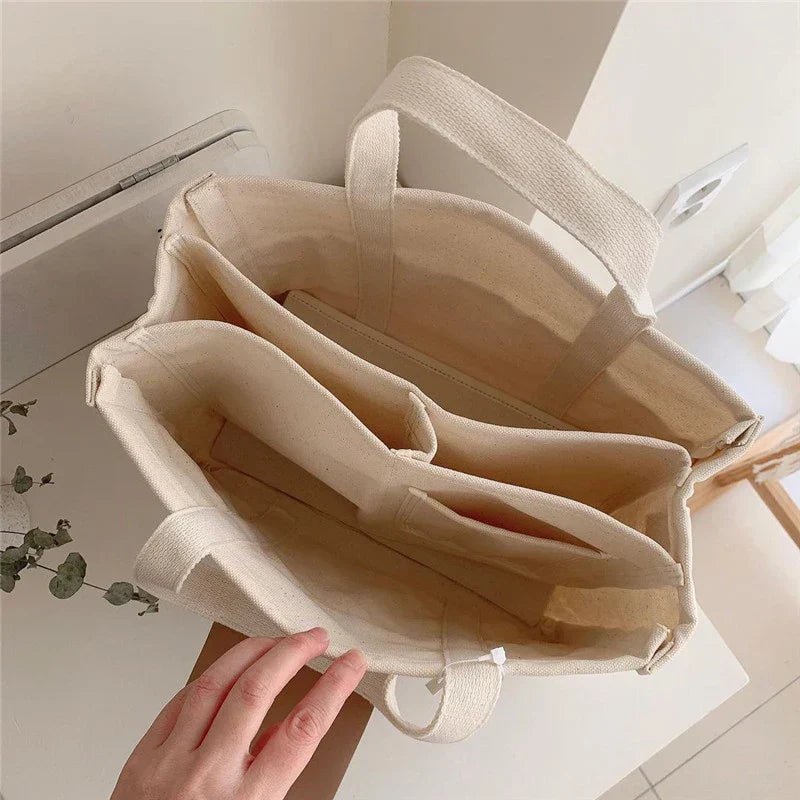 Stylish women's canvas shoulder tote in beige, featuring multiple pockets for organization, great for daily use.