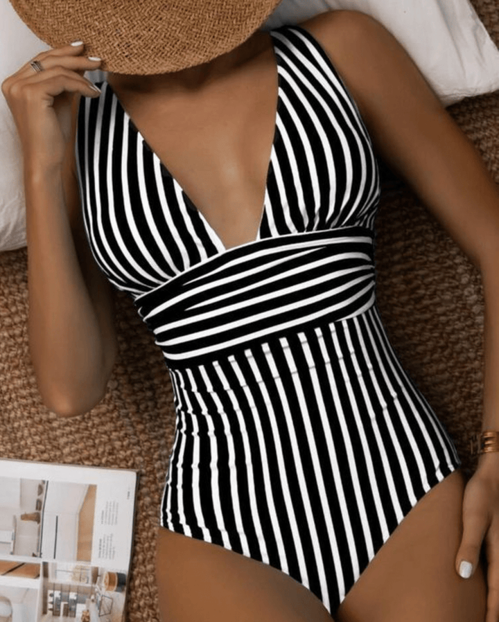 Woman models chic striped one-piece swimsuit, perfect for summer beachwear & poolside style. Flattering fit.