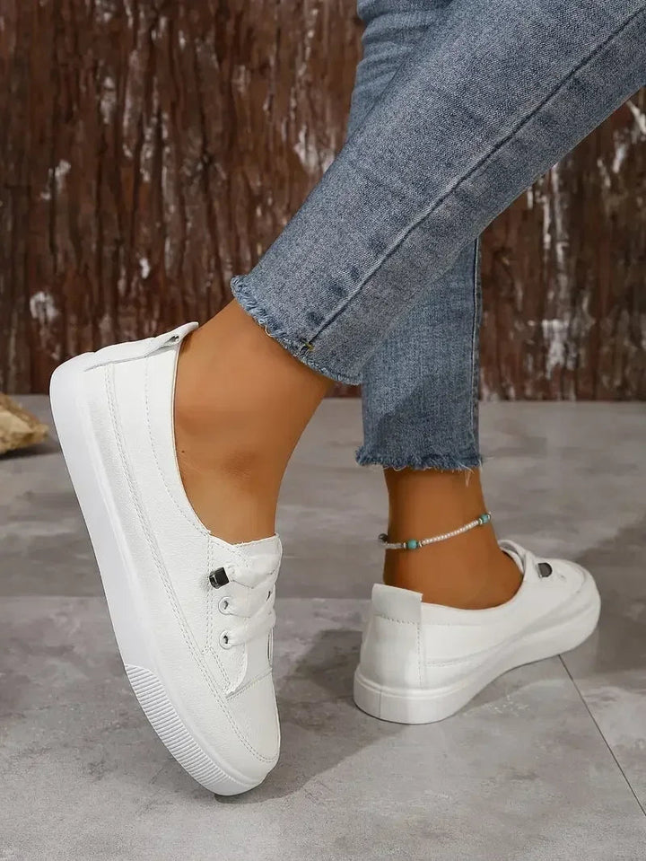 Close-up of white women's casual lace-up sneakers, highlighting the round toe and flat sole.