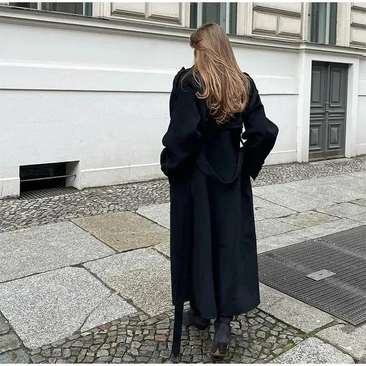 Modern women's black double-breasted longline coat. Oversized winter outerwear offering warmth and style.