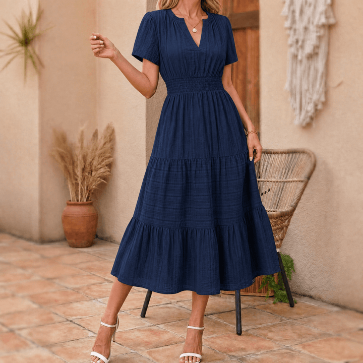 Model showcasing an elegant V-neck tiered midi dress with smocked waist, short sleeves, and pockets.