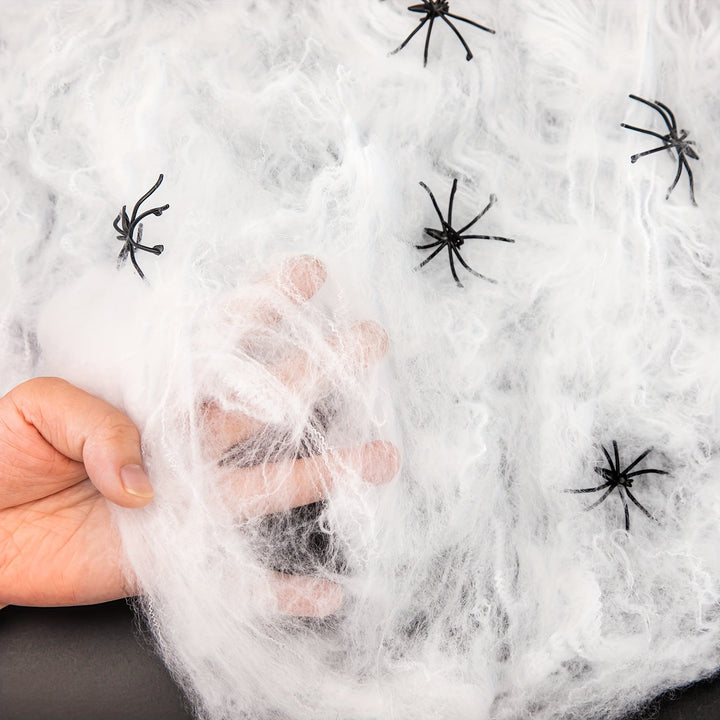 Stretchy white cobwebs draped over a giant Halloween spider web with fake spiders, enhancing spooky party decor.