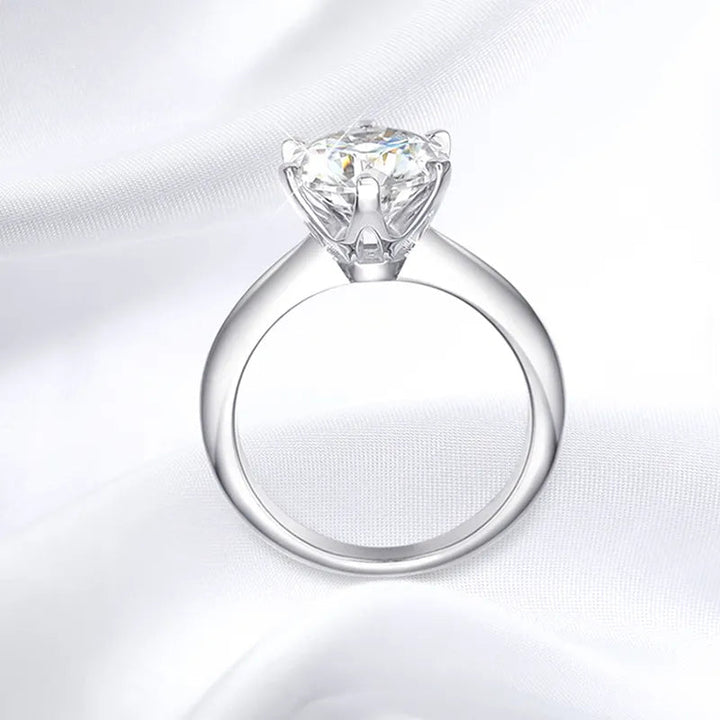 Women's brilliant cut moissanite engagement ring with sterling silver band, shimmering on finger.