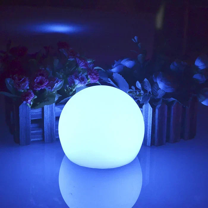 Two GlowSphere LED sphere lights nestled among plants in a garden bed.